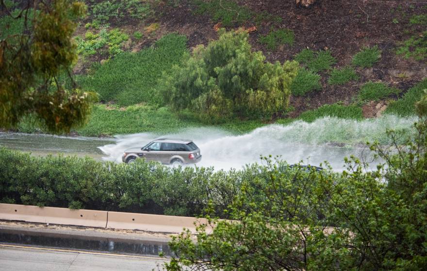 SUV driving a flooded freeway, water splashing behind