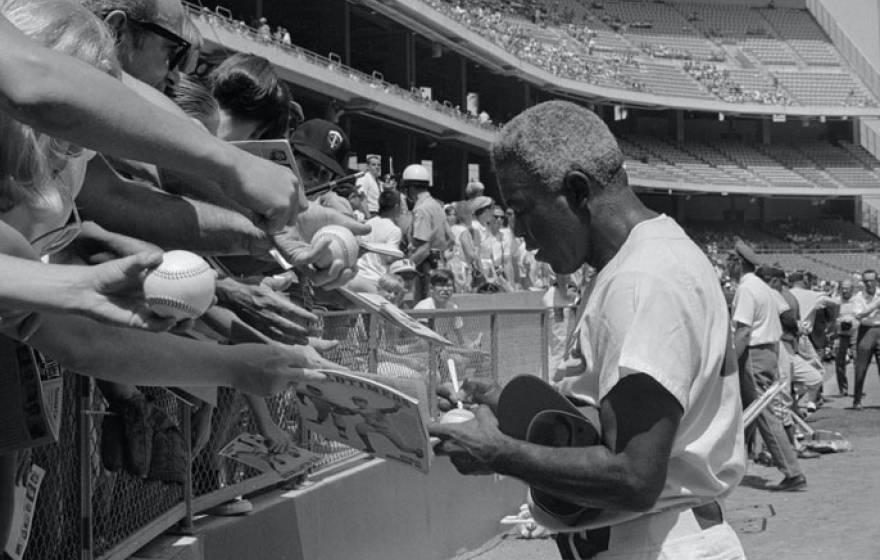 Jackie Robinson signing autographs at a game