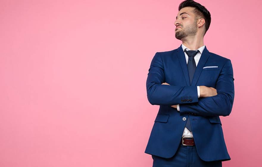 Man in tailored suit with arms crossed looking down with a hint of an attitude