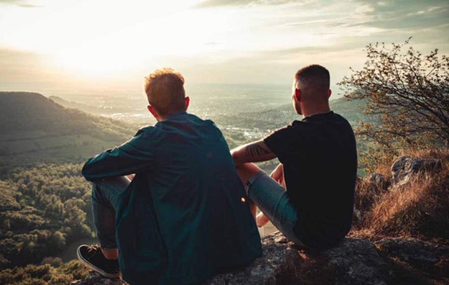 Two men stare down into a sunlit valley