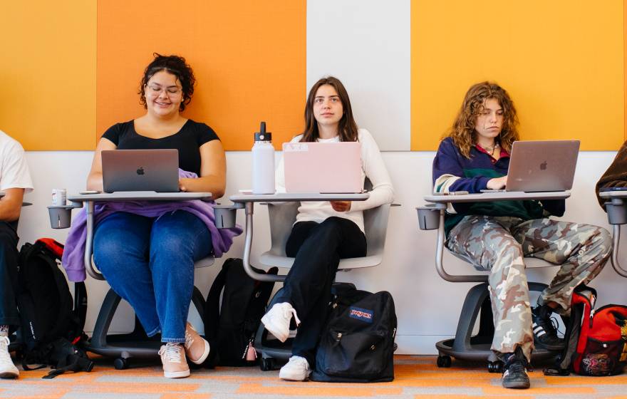 A row of students on laptops sitting at desks in a classroom