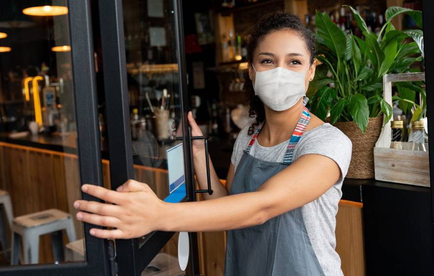 Woman wearing mask opens a cafe door