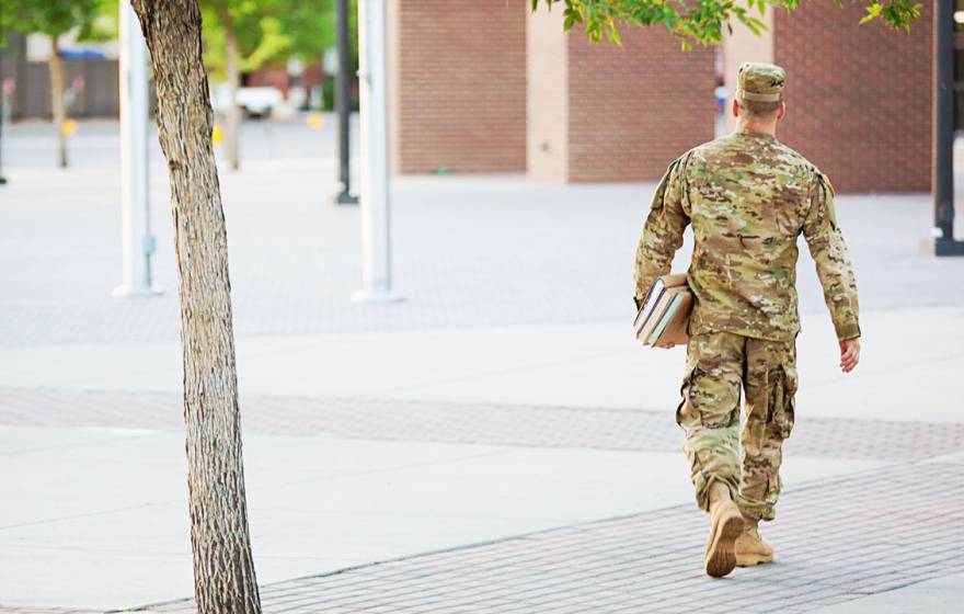 Soldier walks across a campus holding books