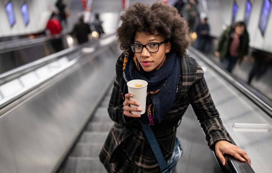 Young woman holding a coffee going up the escalator