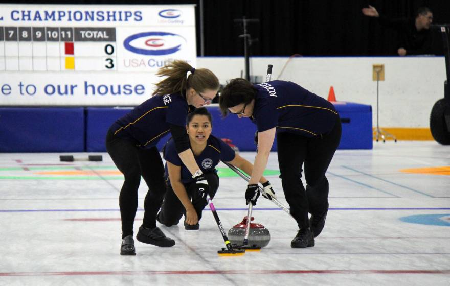 Three women curling, one delivering the stone, two sweeping