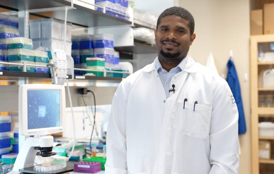 Young Black man with a goatee in a lab coat in a lab, smiling