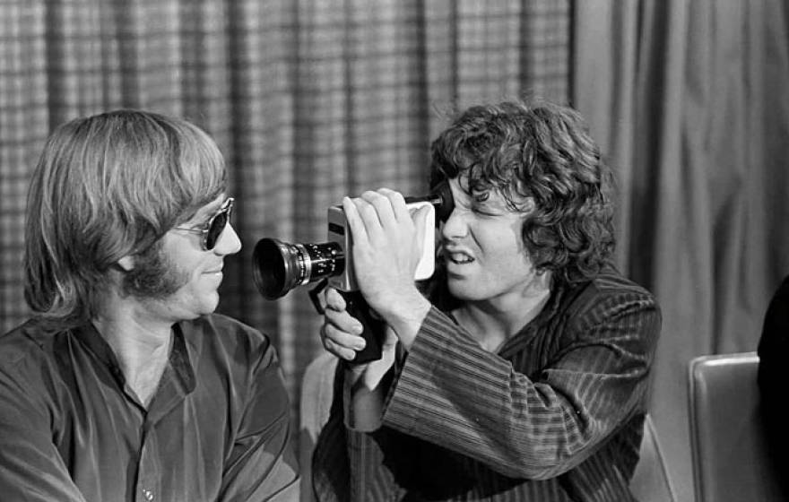 Jim Morrison holding a film camera up to Ray Manzarek