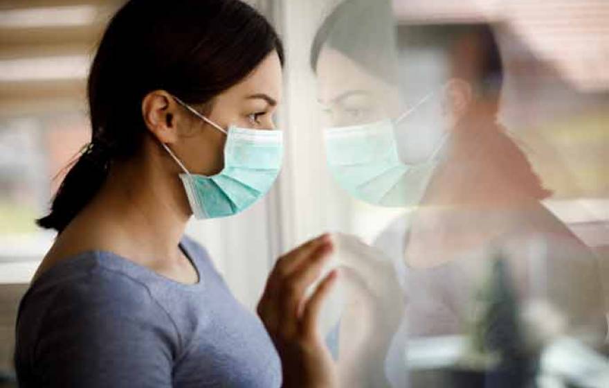 Woman wearing mask looking outside, forlorn