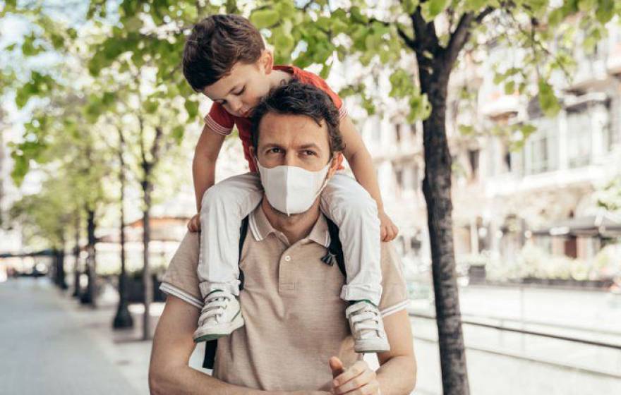 Father wearing a mask carrying a child