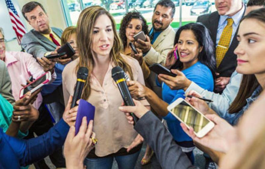 Woman stands in a crowd of microphones