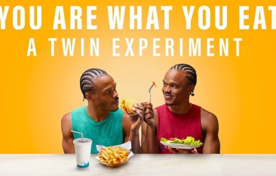 A photo of two young African American men, twins, one eating fast food and the other eating a salad