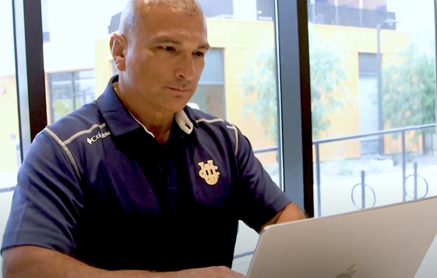 Patrick Acuña, wearing a blue UCI polo and with tattoos on his scalp, types on a laptop.