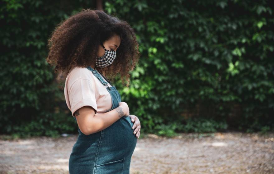 Black pregnant woman cradles stomach outdoors