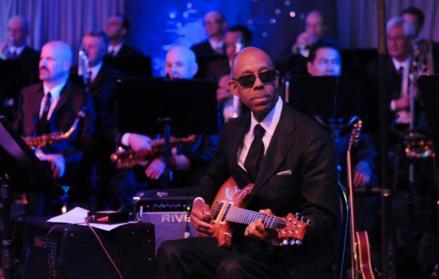 President Drake plays guitar on stage, wearing a black suit and sunglasses