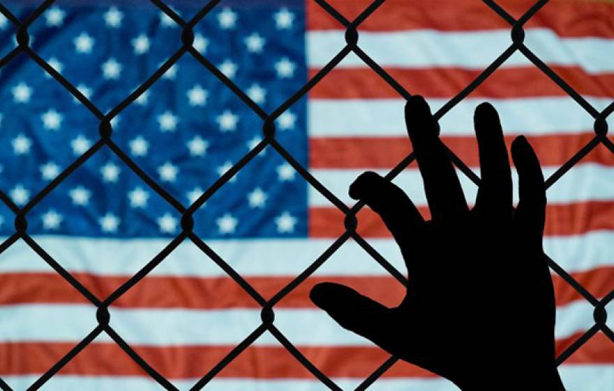Hand on fence in front of an American flag