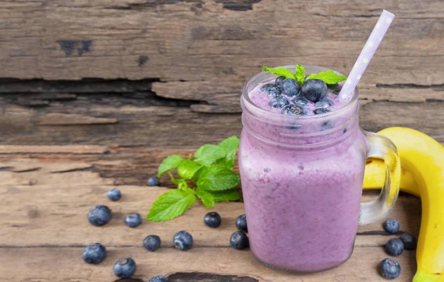 A purple smoothie with blueberries and a banana next to it on a table