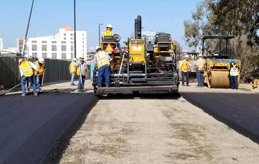 A work crew paves the road with material made of recycled plastic