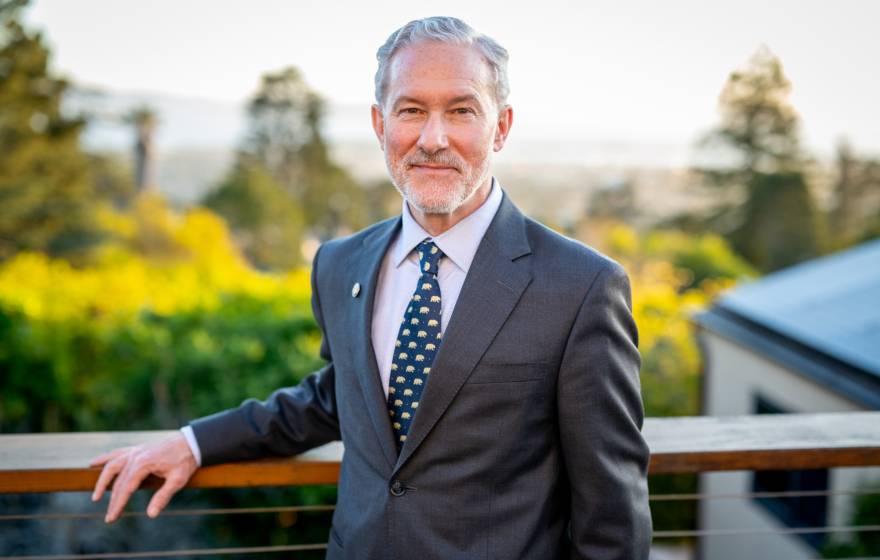 Rich Lyons, a white man with white hair and a white beard, smiling in a suit with a Berkeley bears tie, on campus