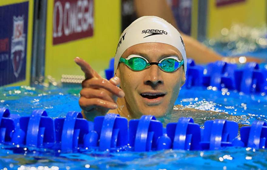 Ryan Murphy pointing from the pool in cap and googles just after a race