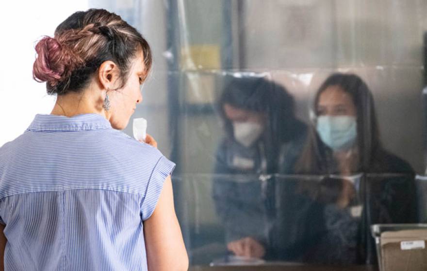 Woman staring through transparent plastic at people wearing PPE