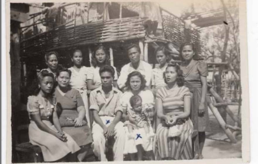 In an old black-and-white photo, a family poses outside