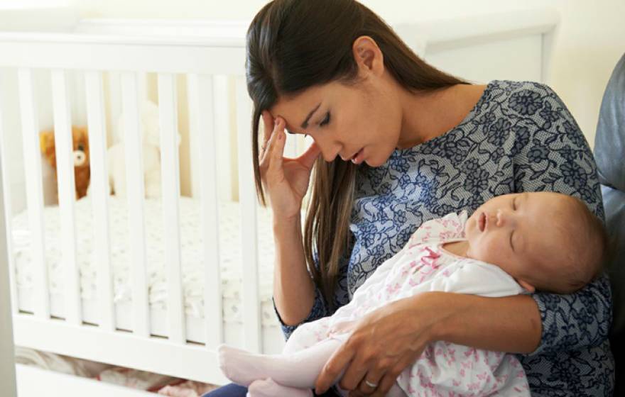 Young mom holds an infant with one hand and her head with the other hand