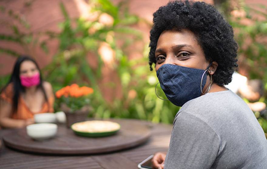 Black woman in mask looks at camera while socializing with friend outside