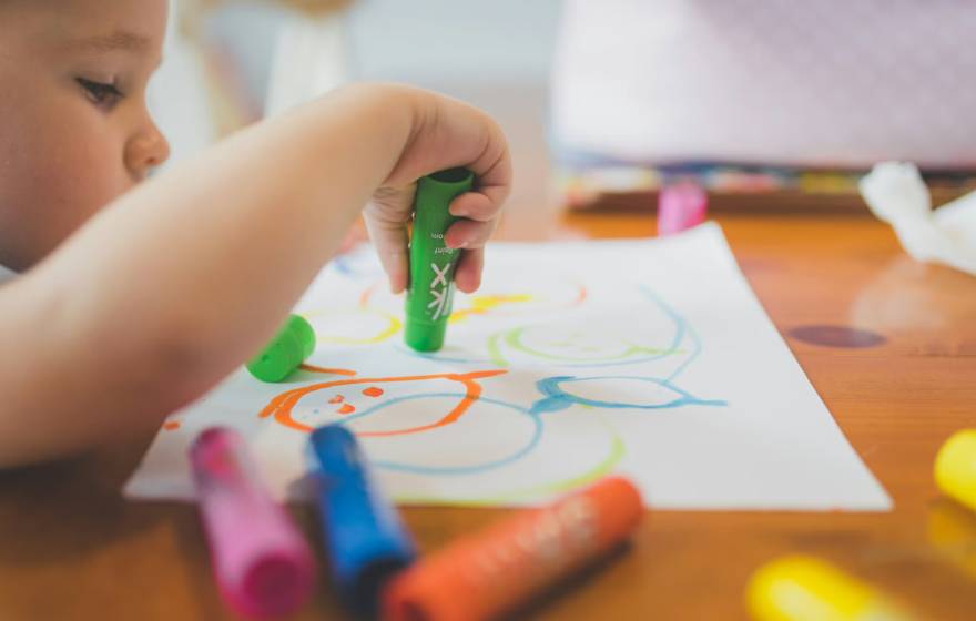 A child at a table draws on a piece of paper with crayons