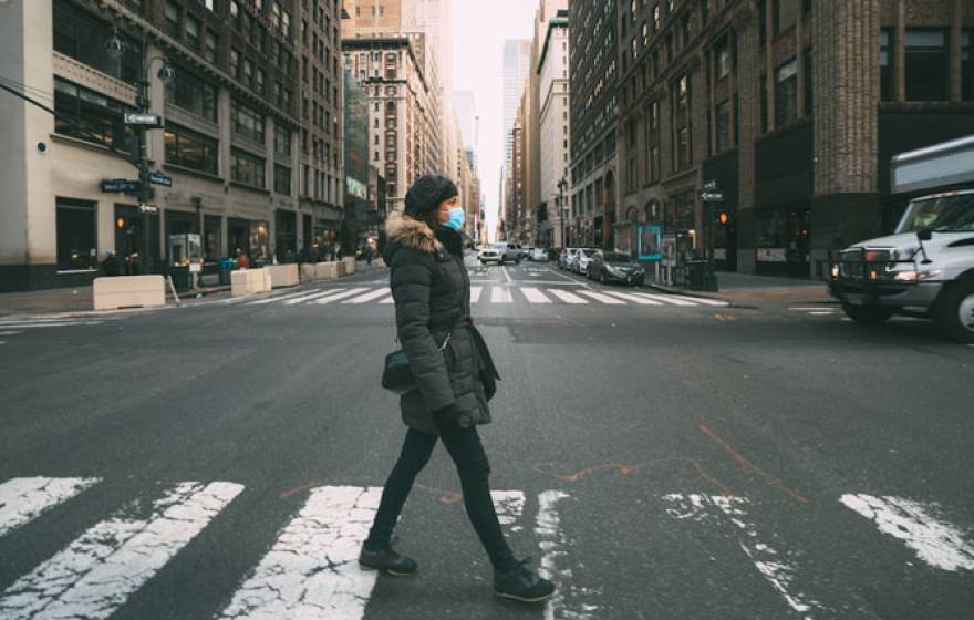 Woman walks down empty city street wearing a mask