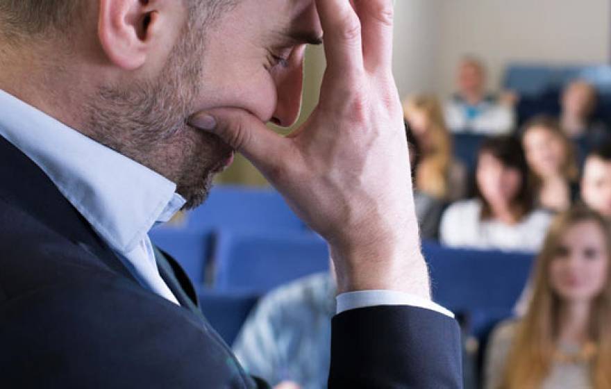 A man in front of a room holding his hand in front of his face in frustration