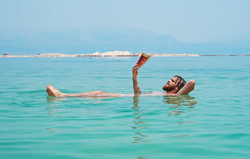 man reads while soaking in a lake