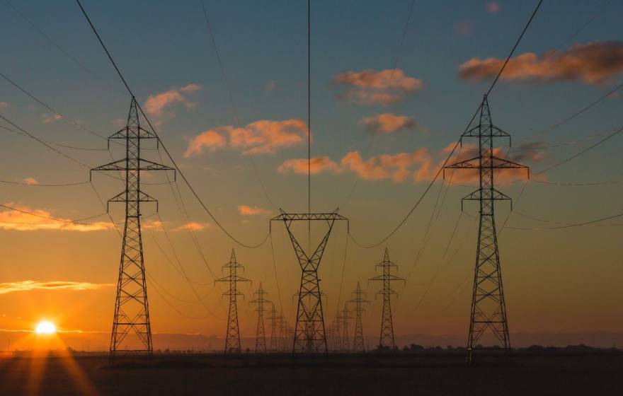 A hazy sunset behind electrical transmission towers, composed symmetrically in frame