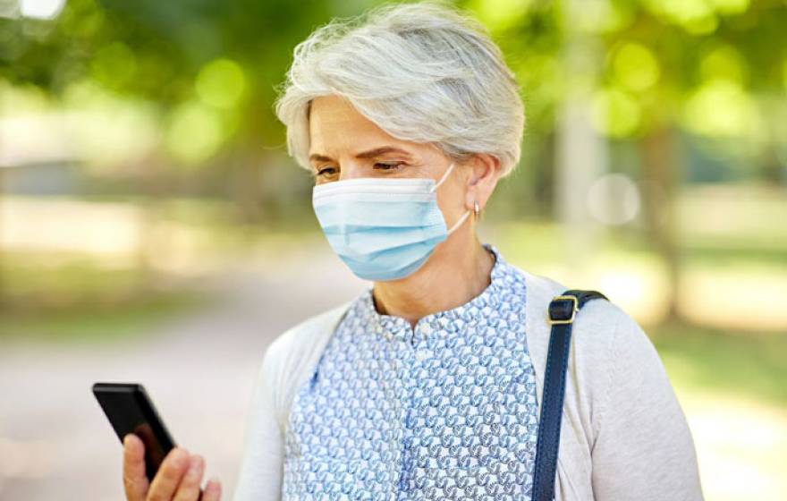 An older woman wearing a mask looks at her phone