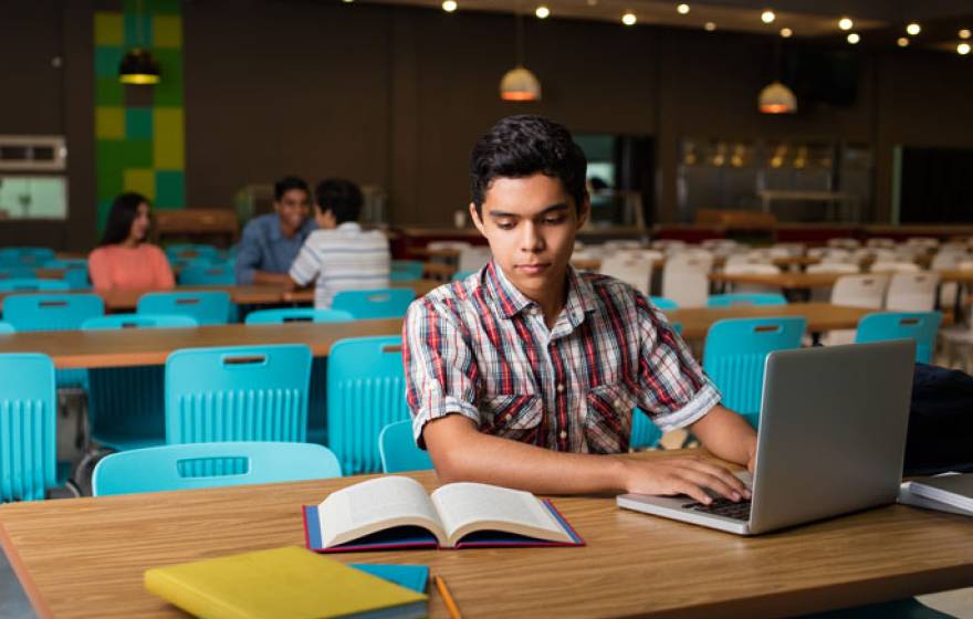 Male student typing on computer from book