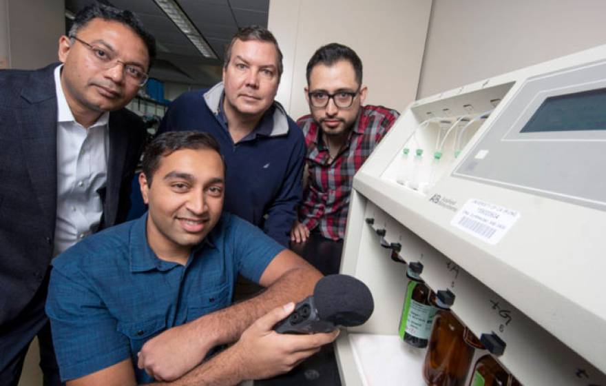 UC Irvine and UC Riverside researchers hold up a microphone to a DNA synthesizer