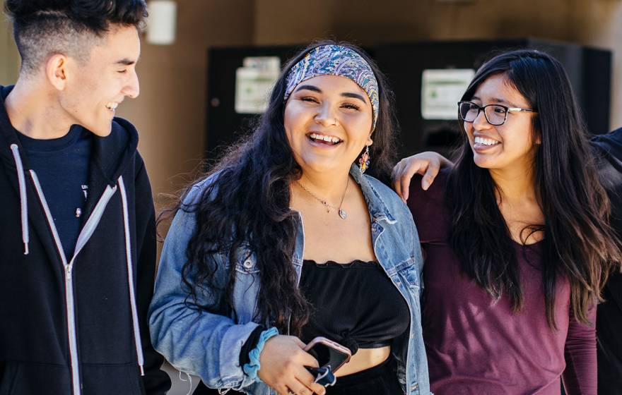 Three students of color smiling and chatting together at UC Merced