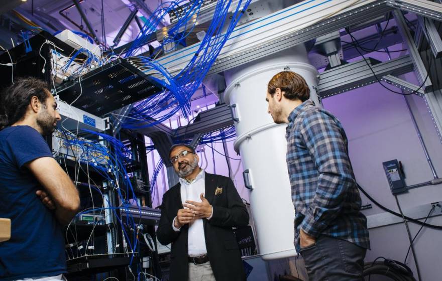 Three men talking in a quantum computing lab with purple lighting