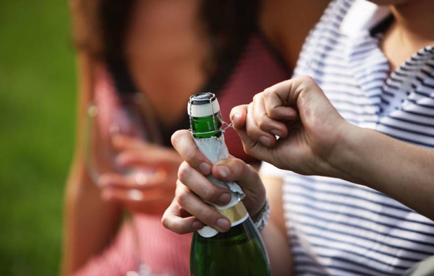 A man opens champagne next to a woman in a park