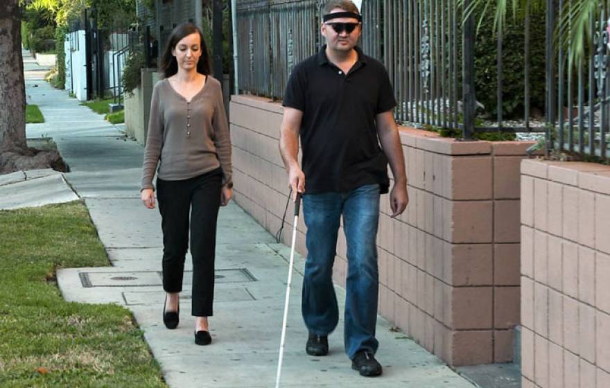 A man with a cane walking with a woman just behind him