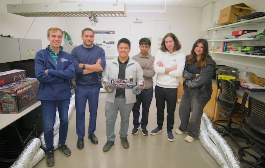 6 people stand in a lab, one holding a small robotic car
