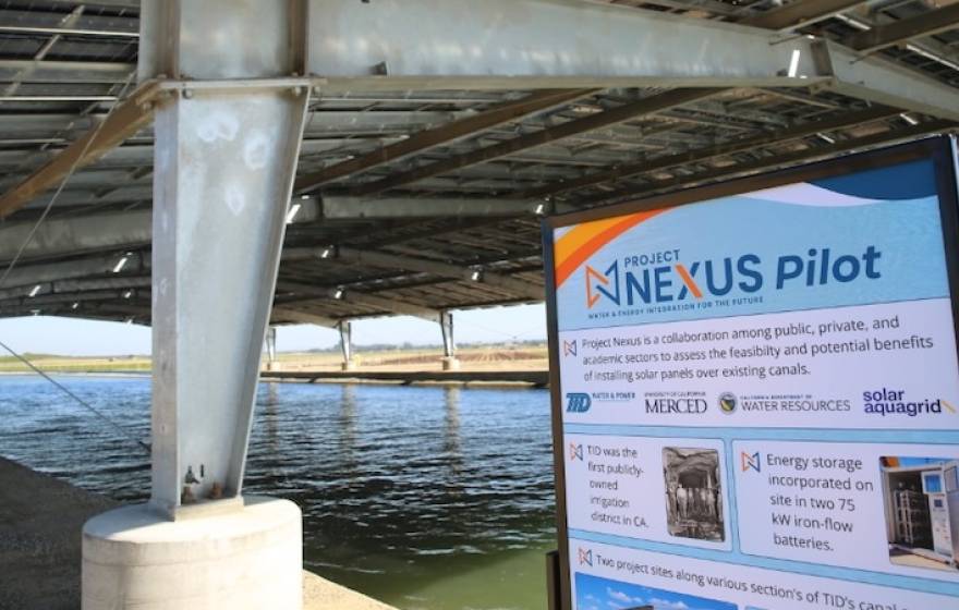 A water canal covered by a solar panel canopy, with a sign for the Nexus project pilot