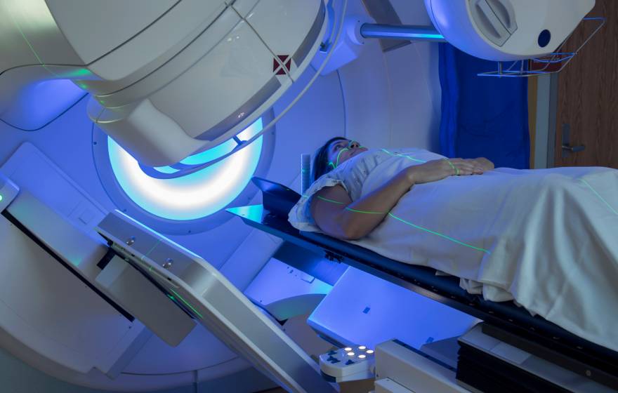 Woman receiving radiation therapy treatments for breast cancer under a machine with green lines of light on her face and body