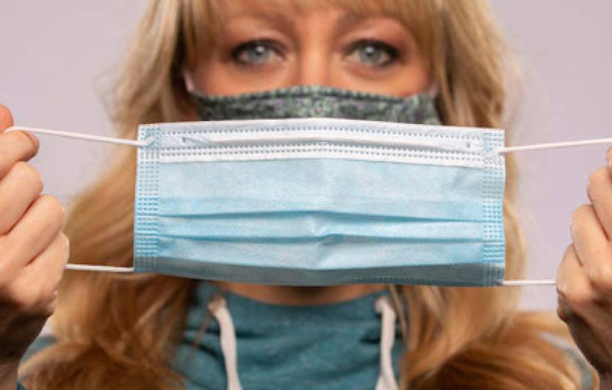 Woman wearing a mask holding up another mask to the camera