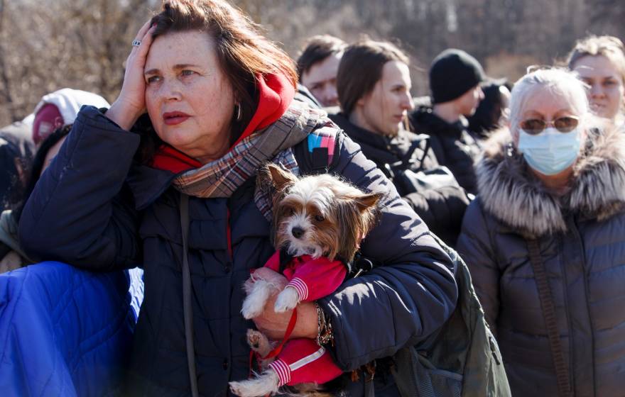 A group of Ukrainian refugees standing outside in winter coats, a middle-aged woman holding a small dog in front