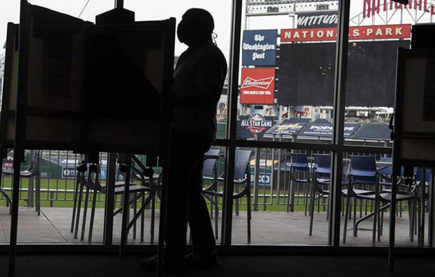 Man at a voting booth, ballpark behind him