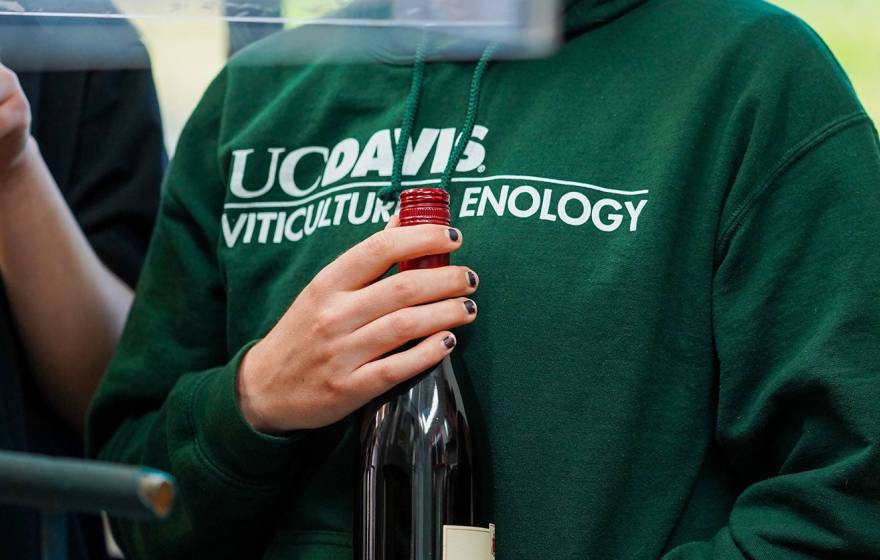 A woman in a green UC Davis viticulture sweatshirt holds a wine bottle