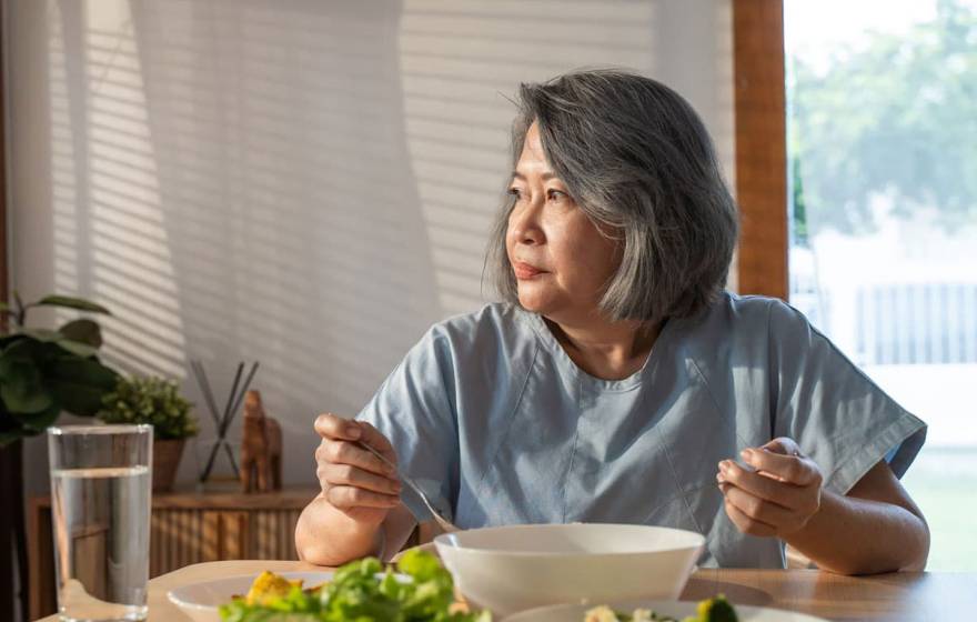 Older Asian woman eating alone, looking wistful