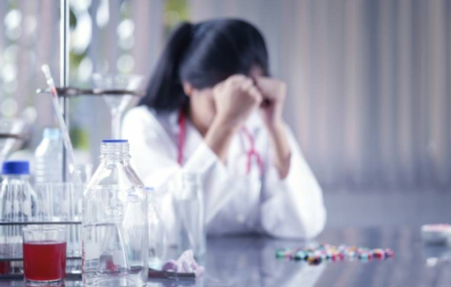 Woman in a lab coat, hangs her head down.