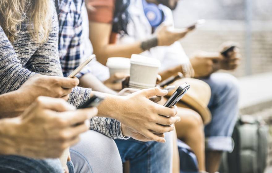 Young adults sitting together on phones no faces visible