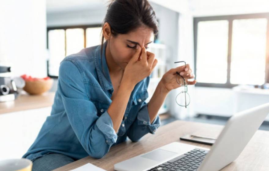 A woman rubs her eyes looking at computer